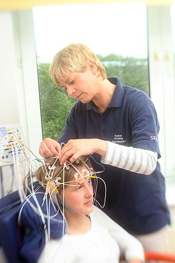 Frau Schneider platziert die Elektroden für ein EEG an bestimmten Punkten am Kopf einer Patientin